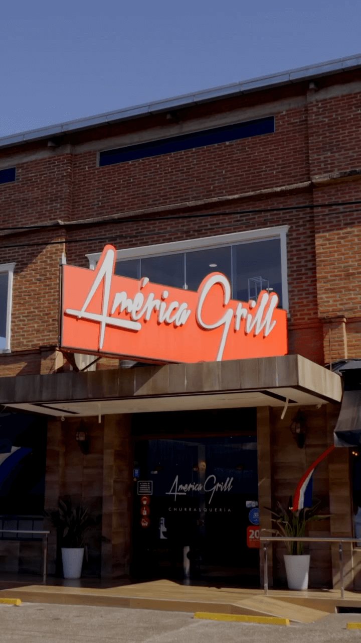 Entrada de América Grill en Encarnación, con su cartel sobre una fachada de ladrillo