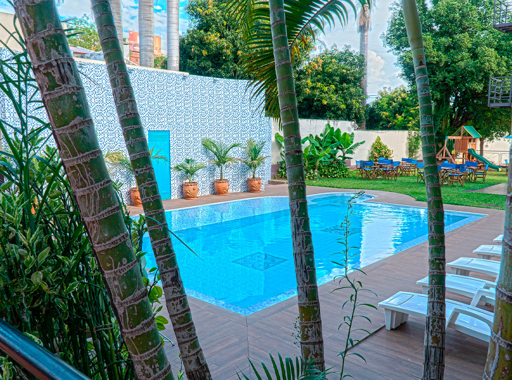Piscina de De La Costa Hotel rodeada de palmeras, jardín y reposeras