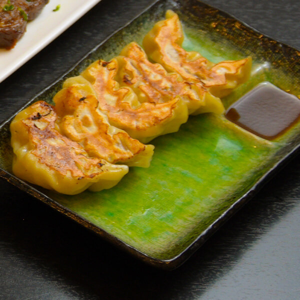 Gyozas doradas, servidas en un plato verde con salsa en Hiroshima